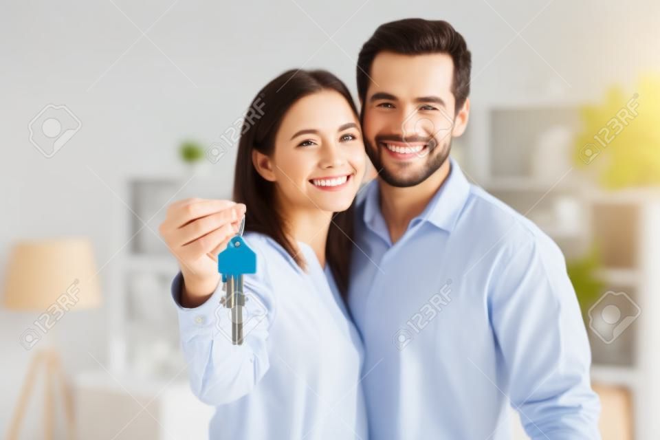 Happy married 30s couple smile look at camera, close up focus to keys bunch from newly bought house. Bank mortgage for young family, start new independent life at own home, housing improvement concept