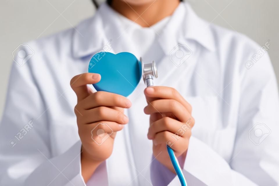 Close up young indian female doctor in white uniform putting stethoscope to heart figure, advertising professional cardiology services, preventing cardiovascular diseases or giving consultation.