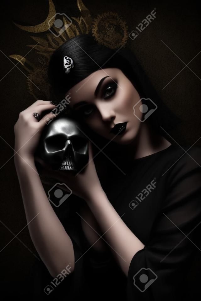 Young woman in black dress in Gothic style posing with skull