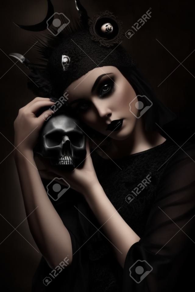 Young woman in black dress in Gothic style posing with skull