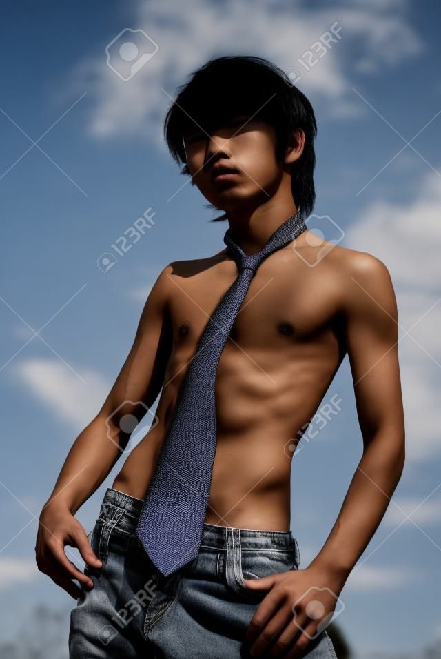 Teenage Asian skinny shirtless boy with necktie and in jeans striking a fashion pose outdoors.