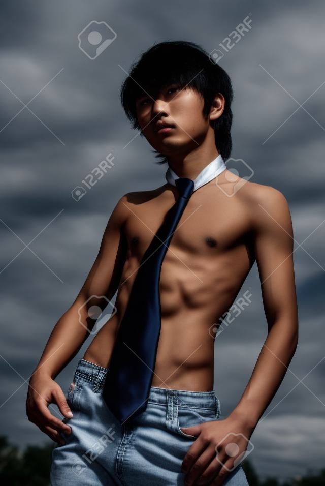 Teenage Asian skinny shirtless boy with necktie and in jeans striking a fashion pose outdoors.