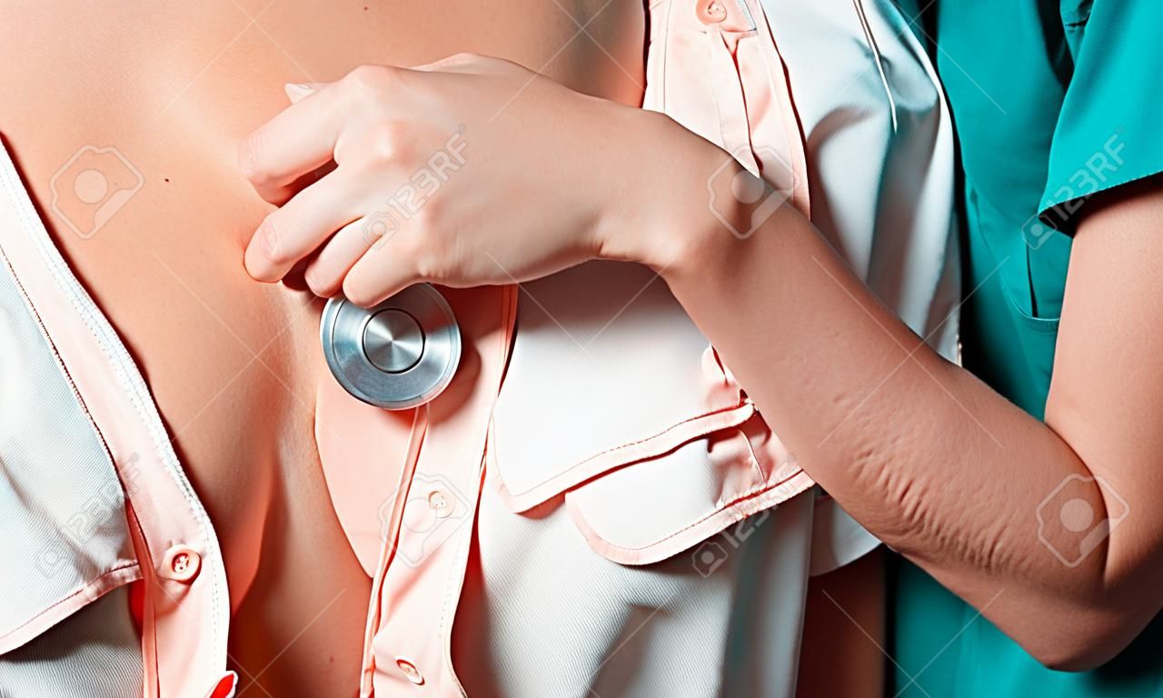 Female Doctor listening to patients chest with stethoscope in medical office