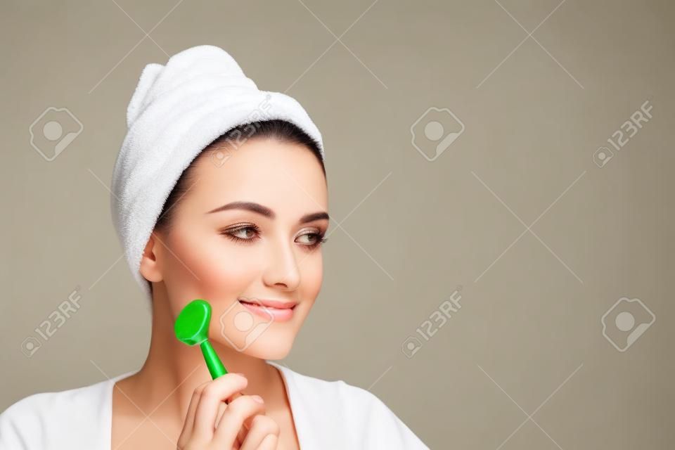 Face massage. Beautiful woman is getting massage face using jade facial roller for skin care, beauty treatment at home