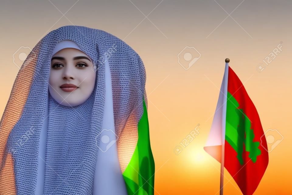 Muslim woman in scarf with Saudi Arabia flag of at sunset.Concept