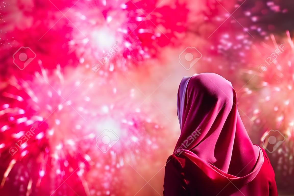 Muslim woman in a red scarf during fireworks at night.