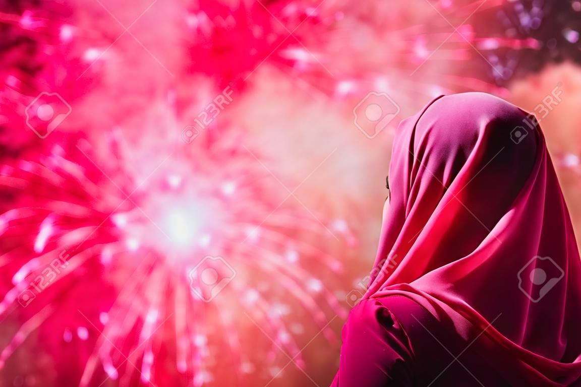 Muslim woman in a red scarf during fireworks at night.