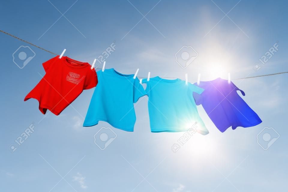 T恤衫挂在蓝色的天空和太阳前面的晾衣绳