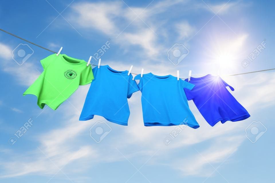 T-Shirts hängen auf einer Wäscheleine vor blauem Himmel und Sonne