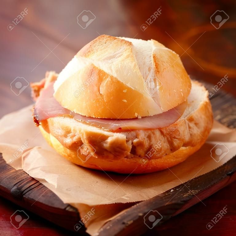 Rolo branco crocante recém-assado e pão de carne de porco e carne bovina alemã servido como um lanche de takeaway em um pedaço de papel marrom amassado, close up view