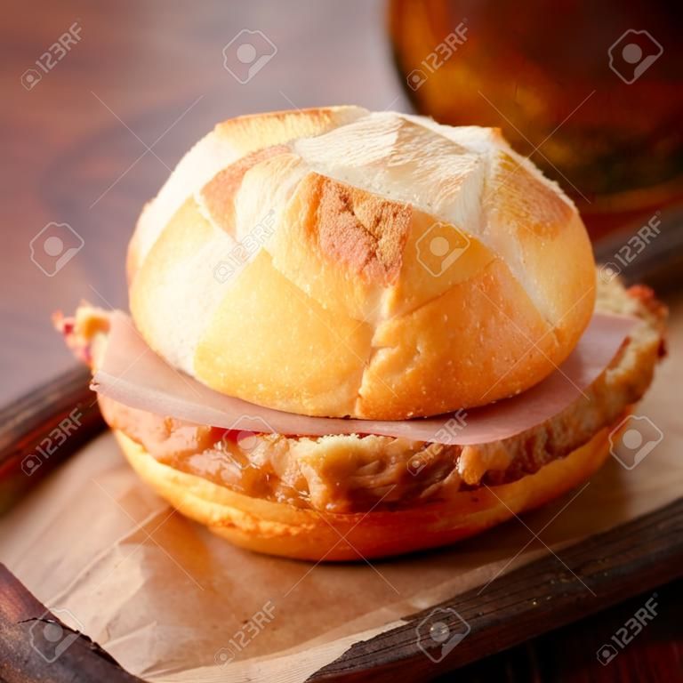 Rolo branco crocante recém-assado e pão de carne de porco e carne bovina alemã servido como um lanche de takeaway em um pedaço de papel marrom amassado, close up view