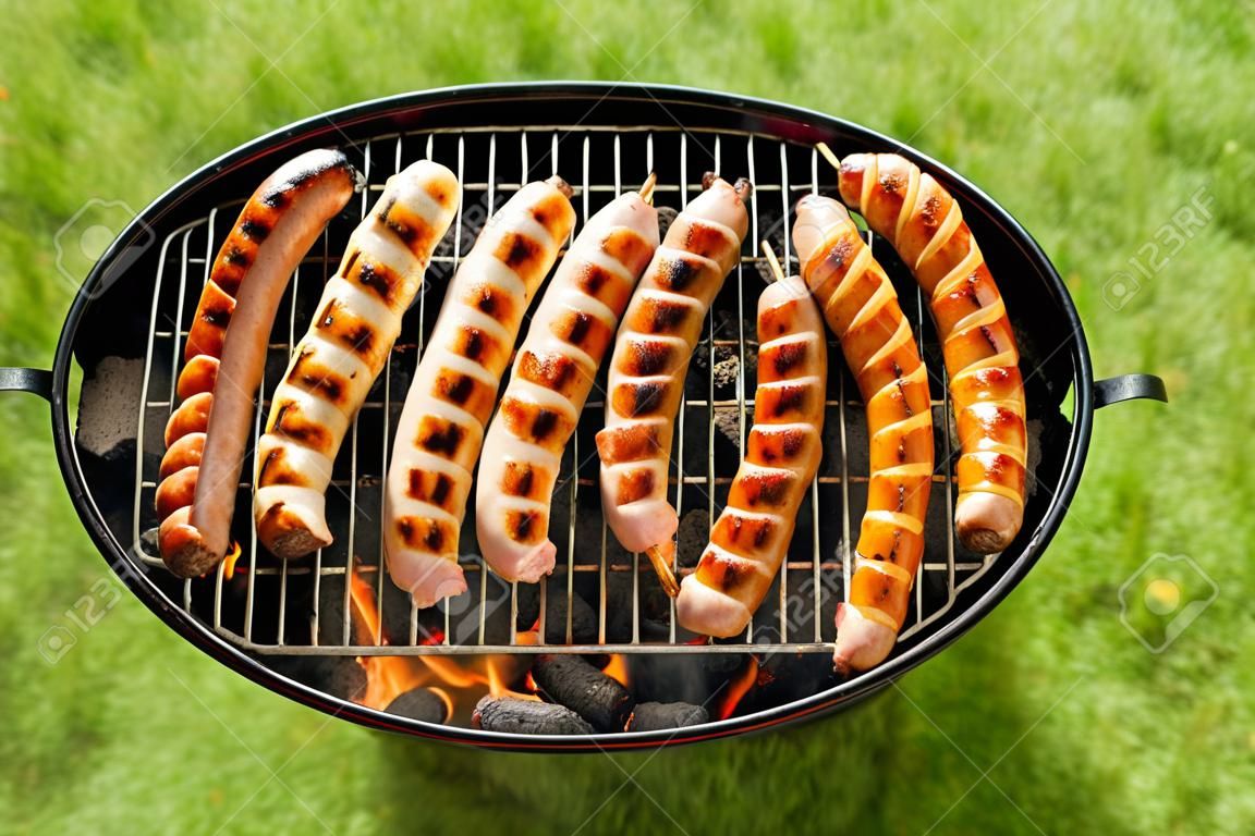 Vista dall'alto su uno sfondo verde erba di una fila di maiale e manzo bratwurst alla griglia sul fuoco barbecue in una giornata calda durante le vacanze estive