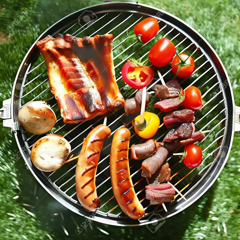 Tasty Sortiment von Fleisch auf einem Sommer-Grill mit Würstchen, Rindfleisch Kebabs und Spare Ribs mit Tomaten und Champignons, Draufsicht über die grünen Gras