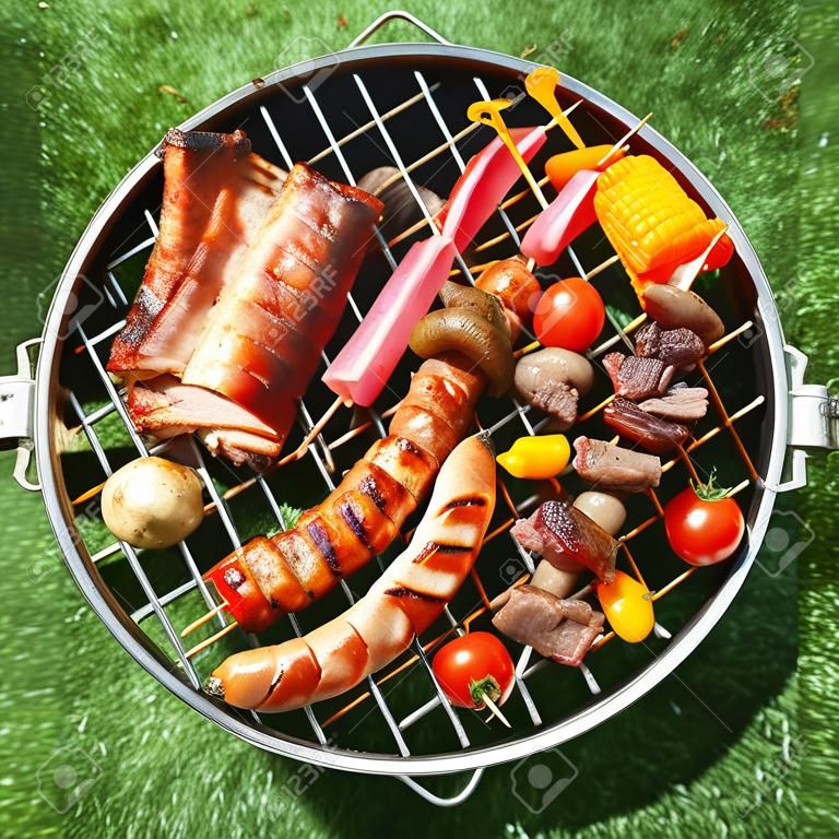 Ízletes választék hús egy nyári grill kolbász, marha kebab és tarja paradicsom és a gomba, általános képet felett zöld fű
