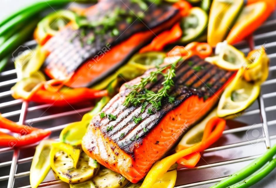 Fresh succulent marine salmon steaks flavored with sprigs of thyme grilling over a barbecue on aluminum foil with sweet pepper and baby carrots