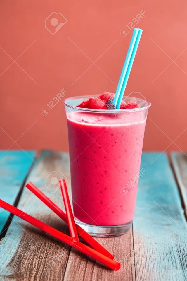 Still Life Profile of Refreshing and Cool Frozen Red Fruit Slush Drink in Plastic Cup Served on Rustic Wooden Table with Collection of Colorful Straws