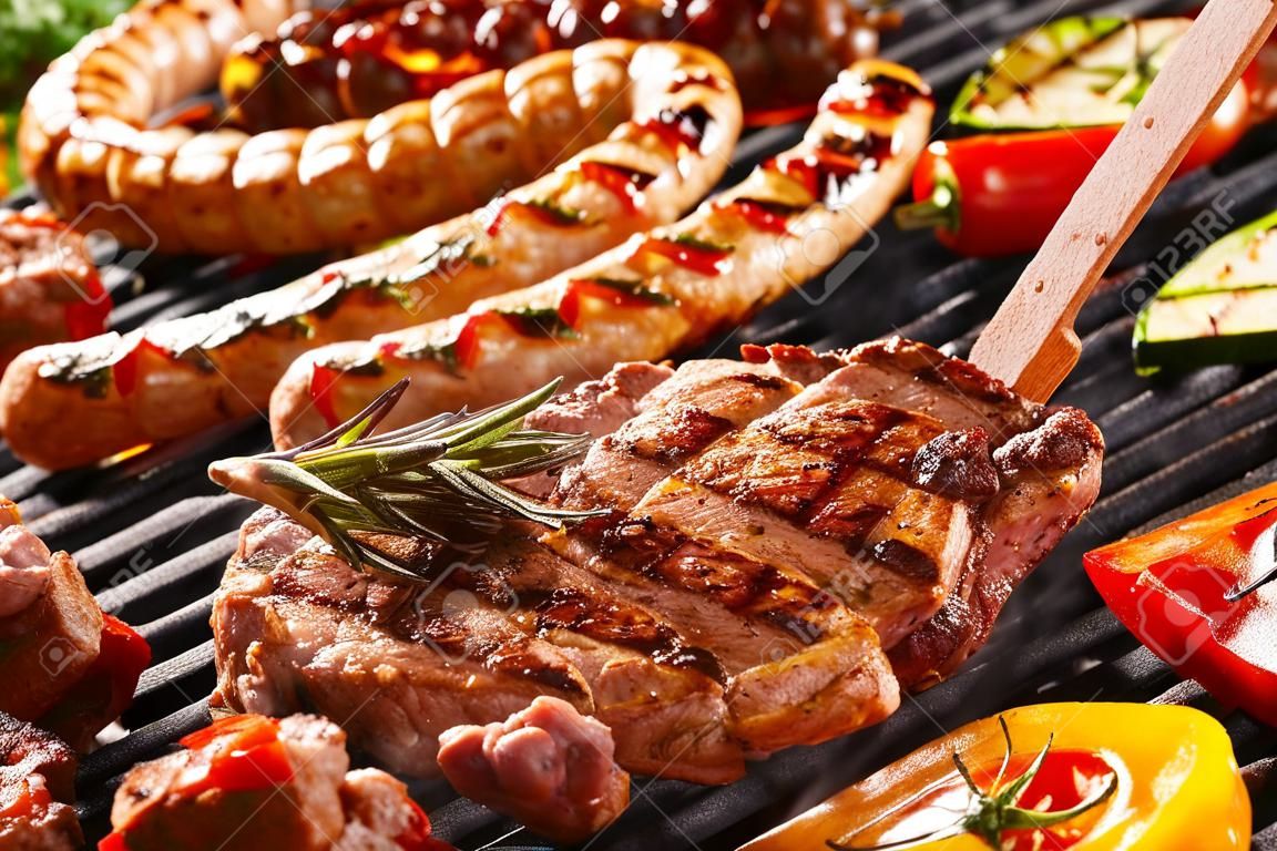 Délicieux assortiment de viande cou steak et des légumes à griller sur un barbecue avec saucisses de porc, côtelettes, brochettes avec des brochettes mixtes, le poivron et l'aubergine dans une vue rapprochée avec des pinces tournant une côtelette