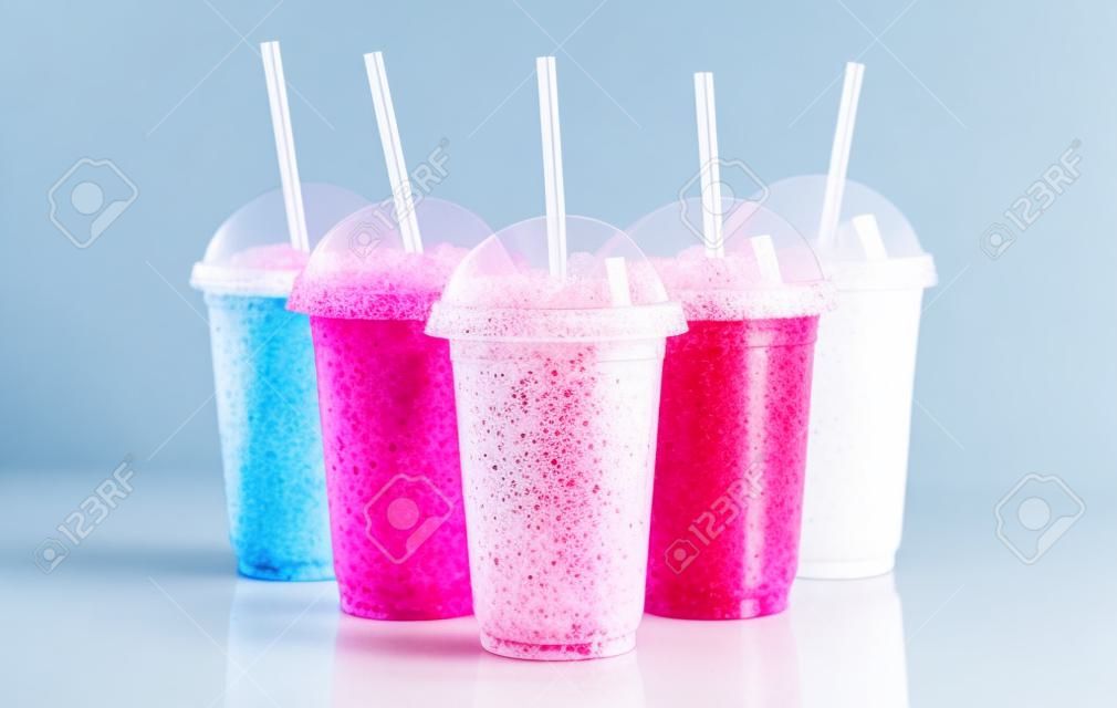 Still Life Profile of Frozen Fruit Slush Granita Drinks in Plastic Take Away Cups with Lids and Drinking Straws Arranged on Reflective Surface in front of White Background