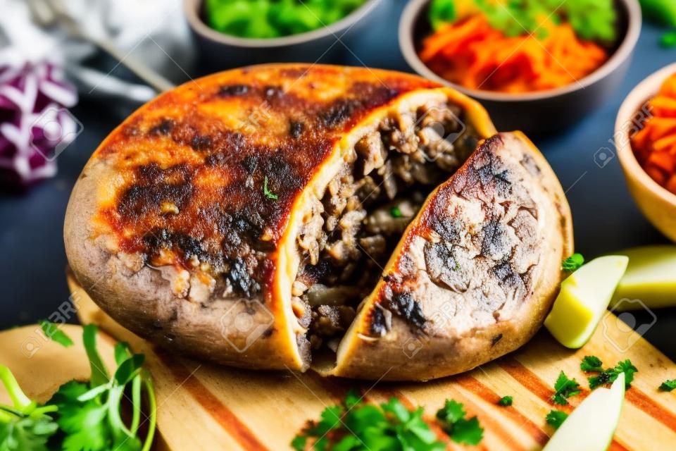 Close up on a sliced open cooked Scottish haggis on a cutting board with side dishes of potato, turnips and carrot, or neeps and tatties