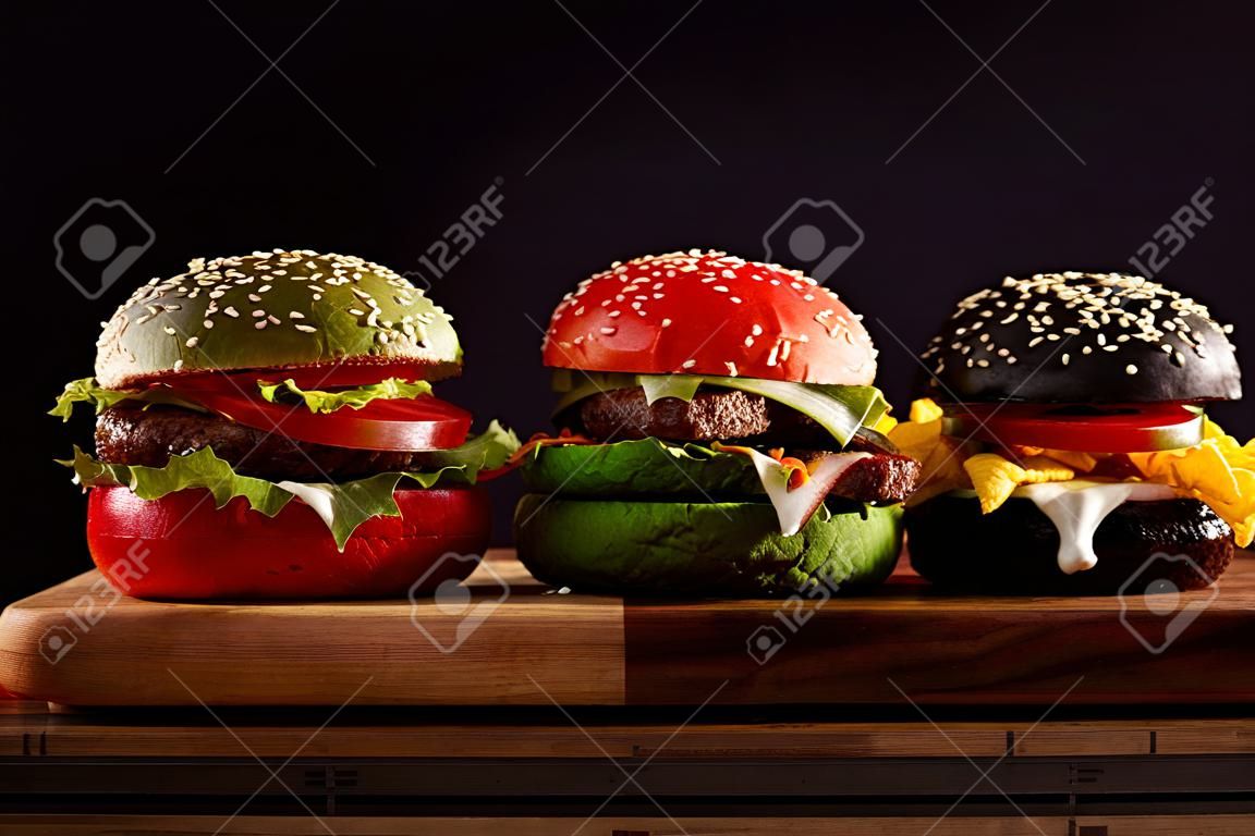 три, гамбургеры на красочных разведенных булочек в красном, зеленом и черном, давая различные варианты заполнения вид сбоку на деревянной доске