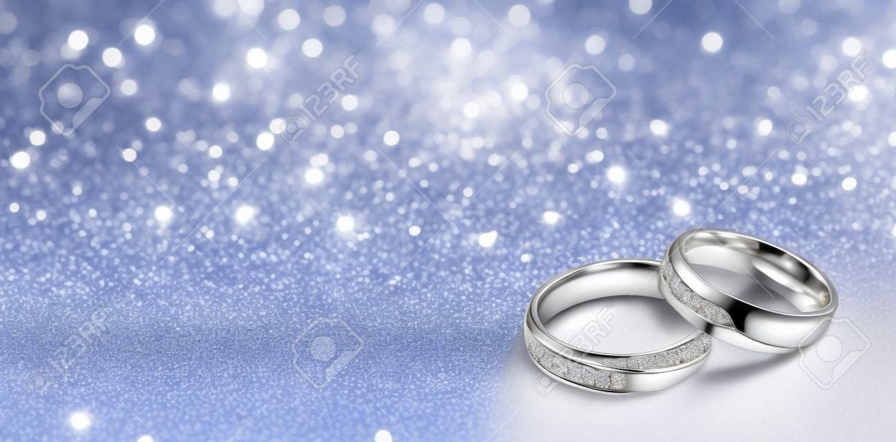 Los anillos de boda de diseño en la esquina sobre un fondo brillante de brillo en formato de banner panorámico con espacio de copia y enfoque selectivo