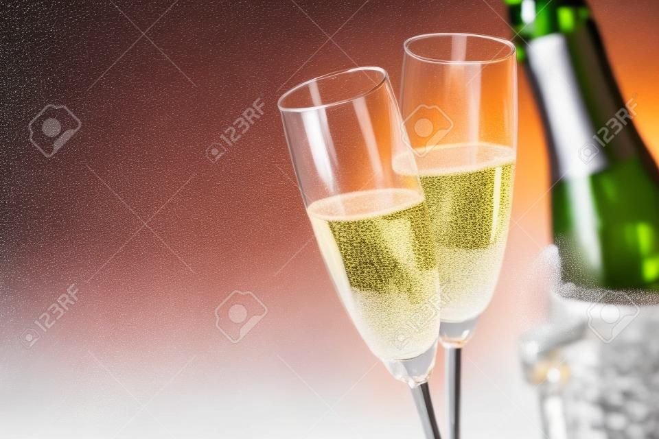 Due bicchieri romantici di champagne frizzante a fianco di una bottiglia in un secchiello del ghiaccio e spazio per celebrare un matrimonio, un anniversario, un capodanno o un giorno di San Valentino