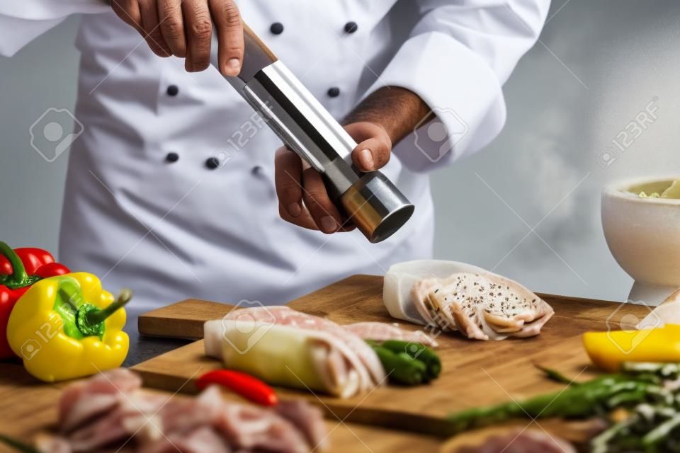 전경에서 야채에 소금에 절인 고기 그물에 대한 흰색 재킷 연삭 후추에 남성 요리사의 측면보기