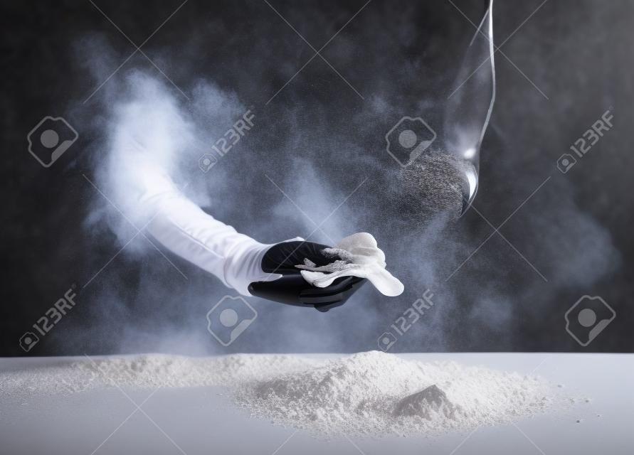 Pracownik restauracji w czarnym garniturze i lateksowych rękawiczkach wycierający białą mąkę w proszku z rąk na prostokątnym