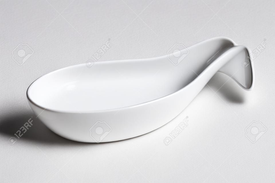 Clean empty white ceramic spoon for food presentation and styling diagonally on a white background with reflection