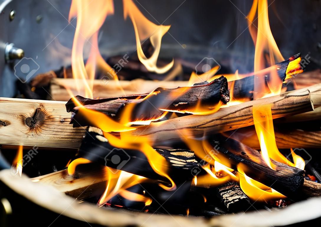 Freshly lit barbecue fire with logs of burning wood over small chips of kindling in a portable BBQ