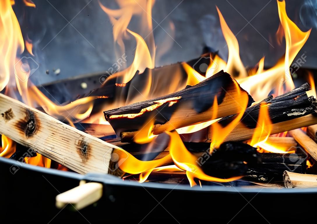 Freshly lit barbecue fire with logs of burning wood over small chips of kindling in a portable BBQ