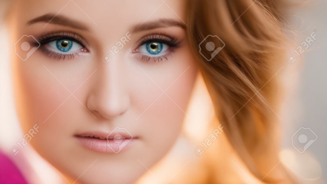 Closeup shoot of young pretty caucasian female with brunette curly hair looking straight at camera with tenderness with bokeh lights on the background