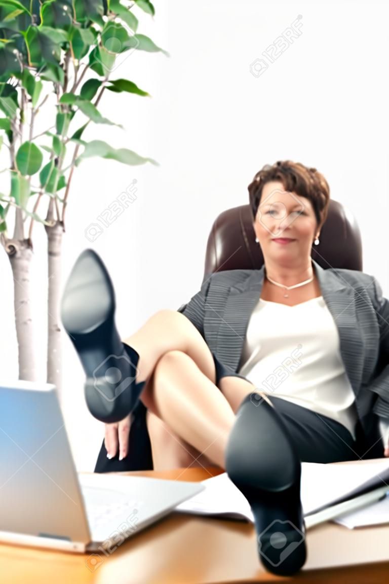 Satisfait, femme d'affaires d'âge mûr à l'aise avec les pieds sur un bureau.