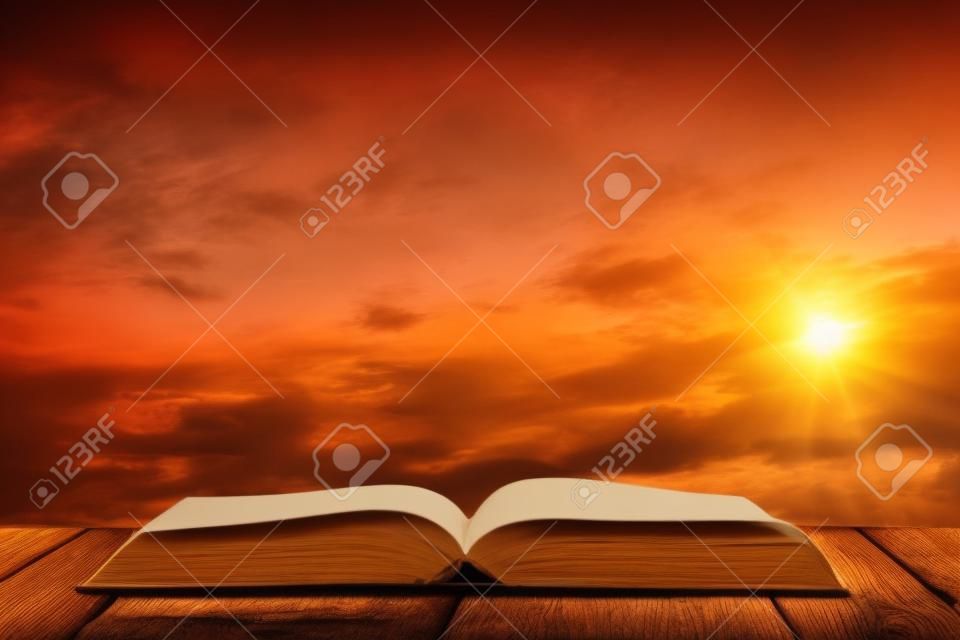 Open book on wood table and sunset as background