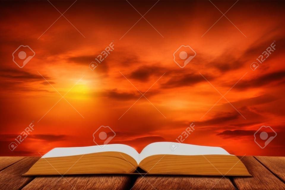 Abrir el libro en la mesa de madera y la puesta del sol como fondo