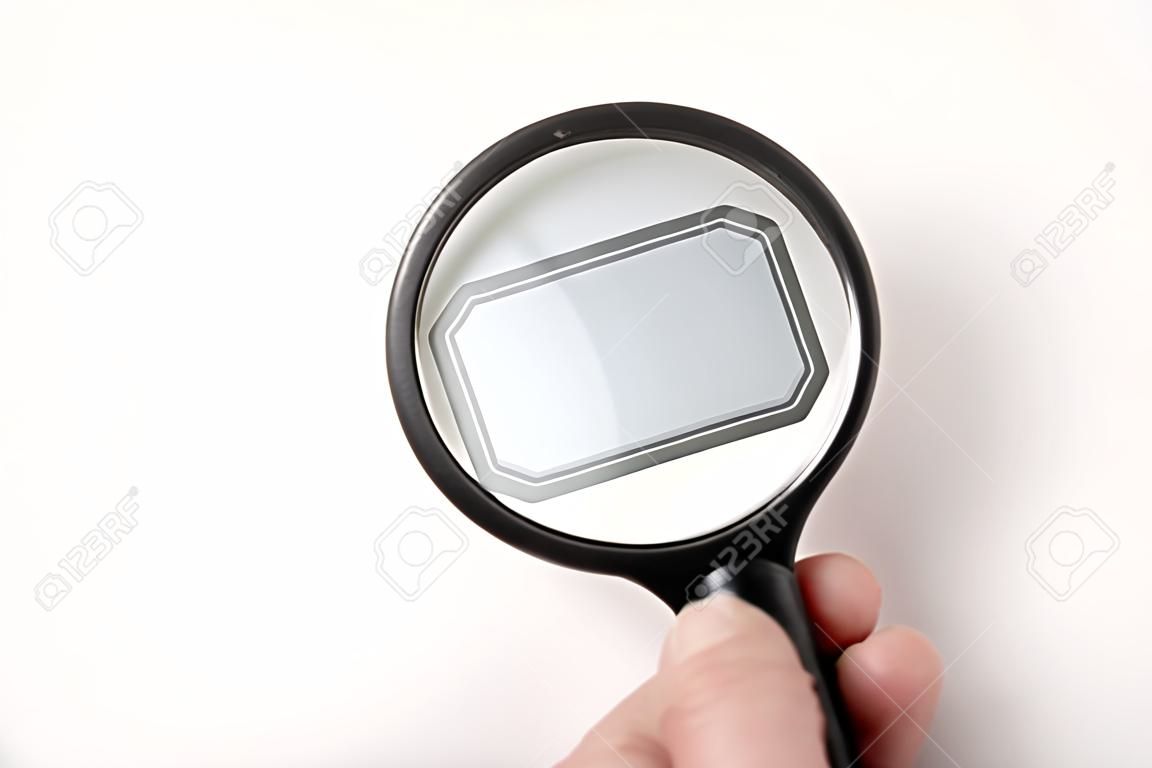 Person hand holding black traditional magnifying glass and looking empty tag, white background. Fill in yourself.