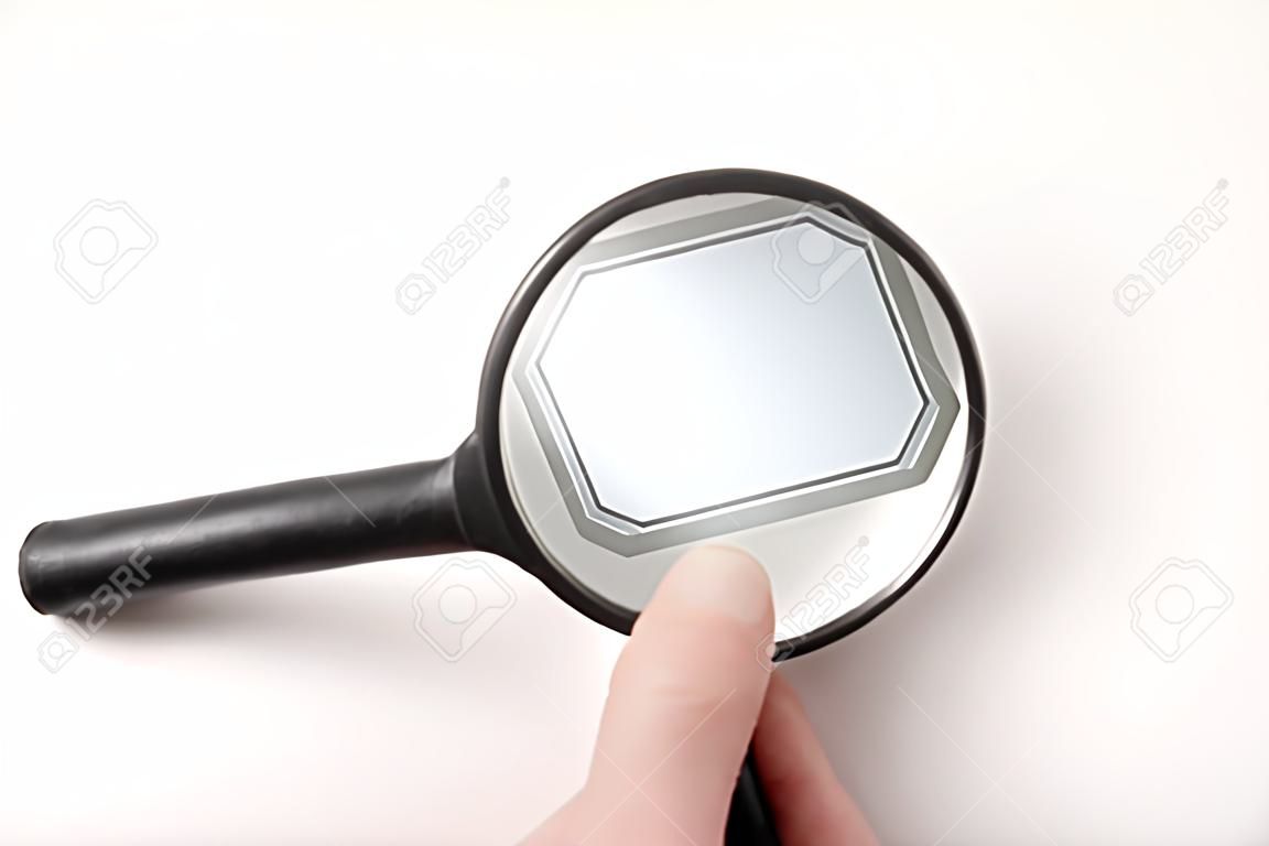 La mano della persona che tiene la lente d'ingrandimento tradizionale nera e guarda lo sfondo bianco dell'etichetta vuota riempi te stesso