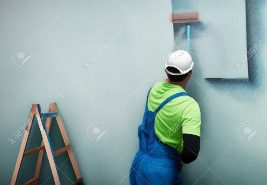 Hombre joven en la pared de la pintura con rodillo