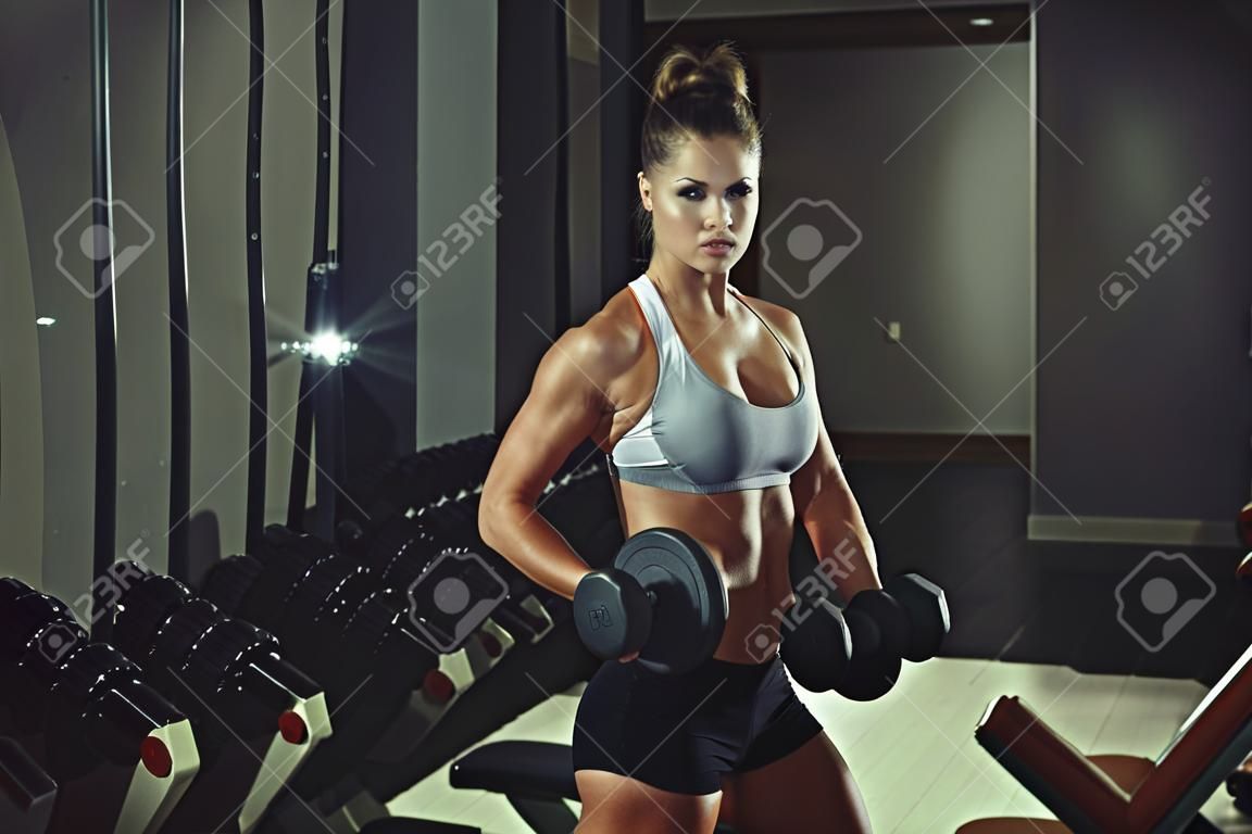 photo de athlétique jeune fille faisant une séance d'entraînement de remise en forme avec des haltères dans le gymnase
