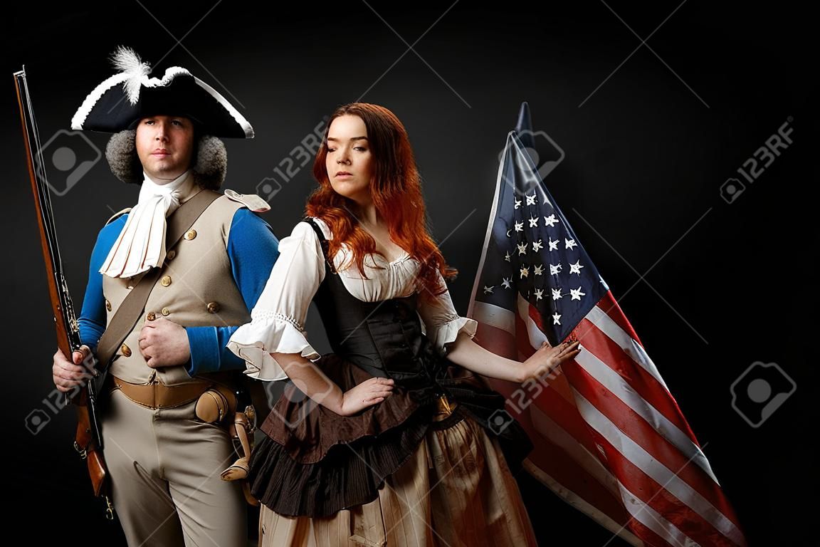Man in de vorm van officier van de Amerikaanse Onafhankelijkheidsoorlog en meisje in historische jurk van 18e eeuw. 4 juli is US Independence Day. Studio foto op zwarte achtergrond