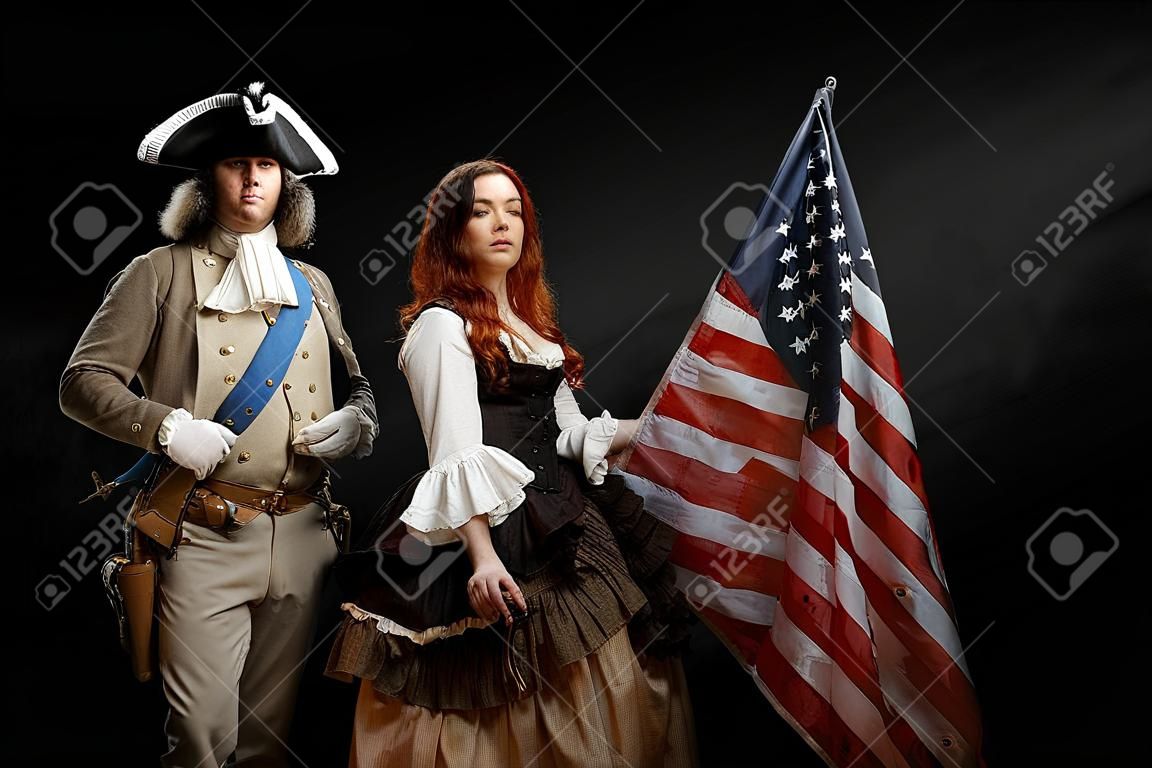 Uomo in forma di ufficiale della Guerra d'Indipendenza degli Stati Uniti e ragazza in abiti storici del XVIII secolo. Il 4 luglio è il Giorno dell'Indipendenza degli Stati Uniti. Foto in studio su sfondo nero