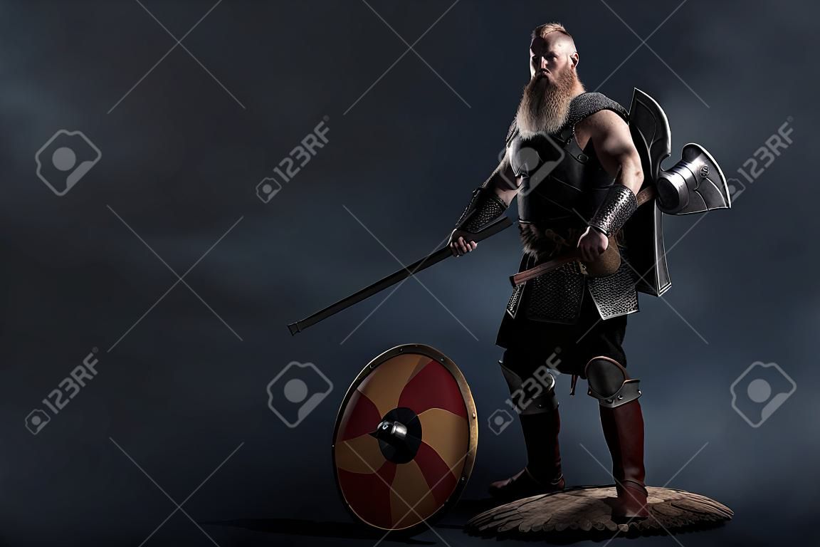 Medieval warrior berserk Viking with axes attacks enemy. Concept historical photo of Scandinavian god in armor and helmet with horns