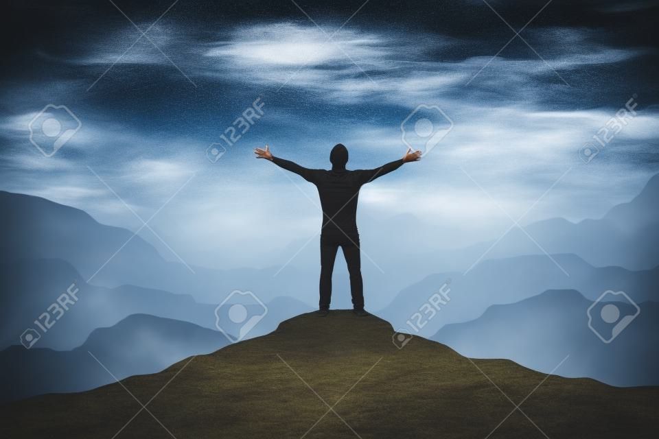 L'uomo in piedi sul bordo della montagna si sente vittorioso con le braccia in aria.