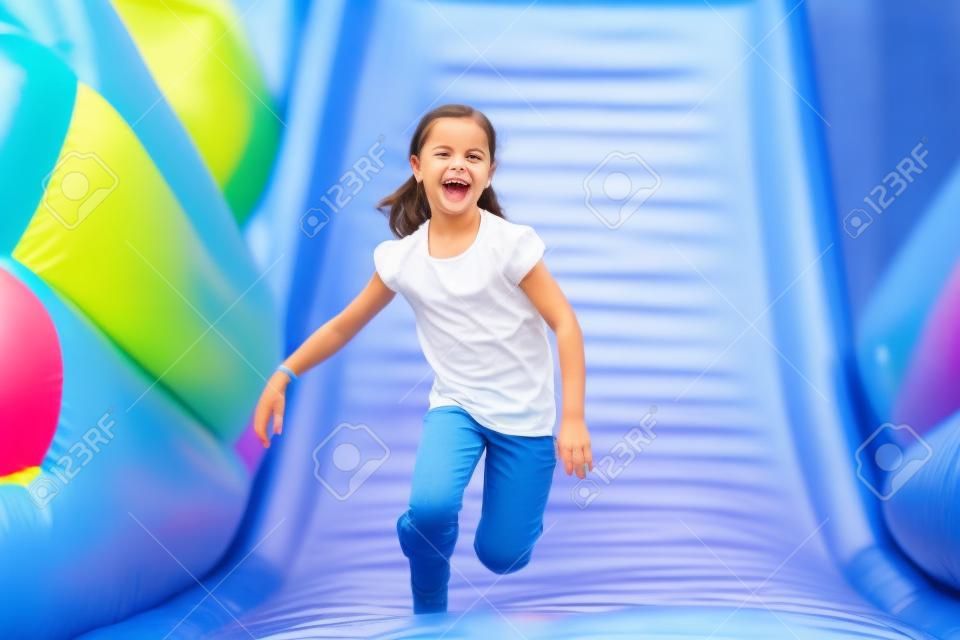 快乐的小女孩有很多乐趣在一个跳跃的城堡，而滑动