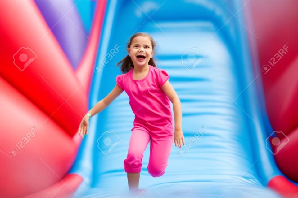 Happy little girl having lots of fun on a jumping castle while sliding.