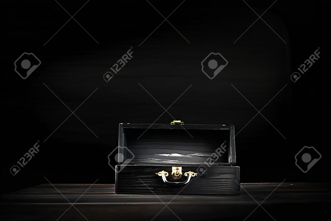 un cofre de madera oscura con tapa abierta y iluminado en superficie de tablón con fondo de pizarra negra .