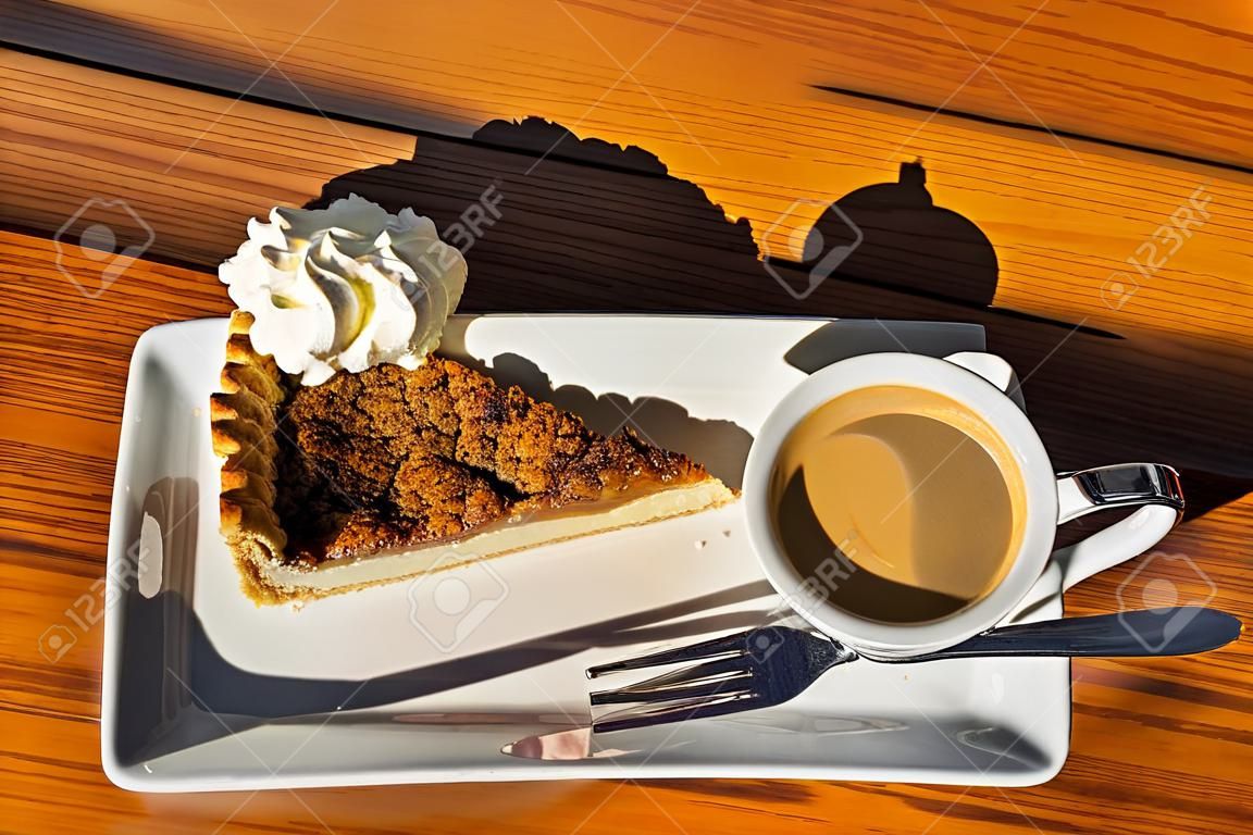 Sun shining on and casting shadows of a square white plate with a cup of black coffee and a piece of apple pie with whipped cream