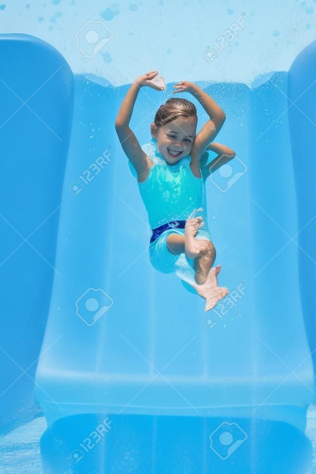 una joven chica linda bajando un tobogán de agua con sus manos sobre su cabeza y doblado en forma de corazón