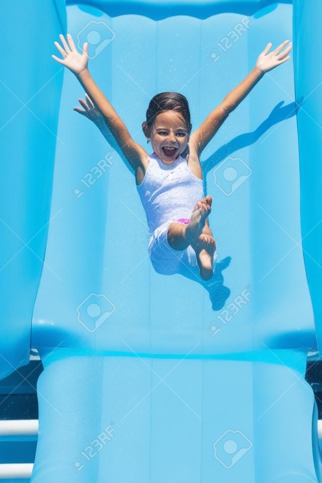 una niña bajando por un tobogán de agua, con los brazos abiertos en el aire y una bonita expresión feliz