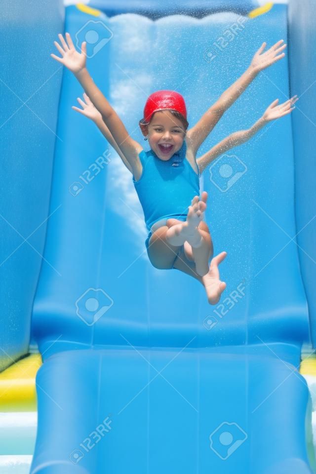 una niña bajando por un tobogán de agua, con los brazos abiertos en el aire y una bonita expresión feliz
